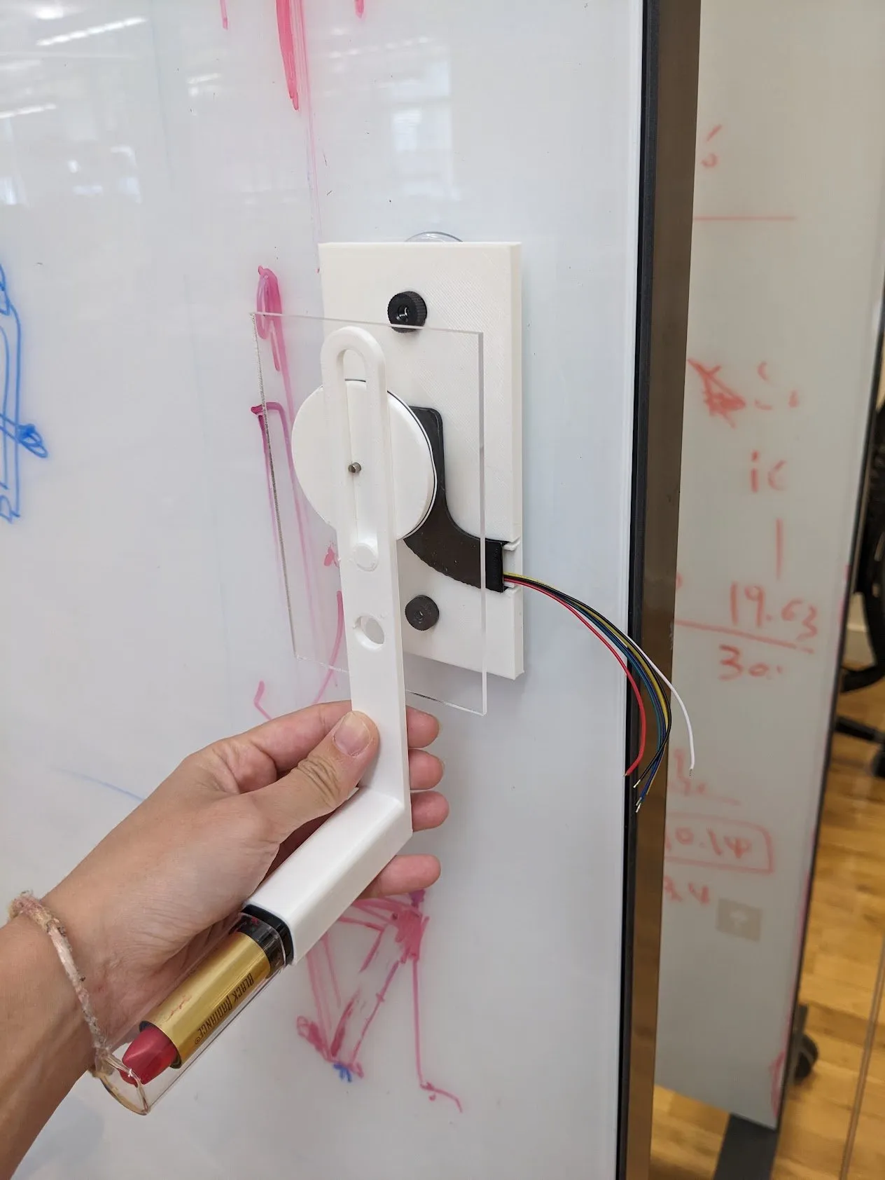 The suction cup mount stuck to a glass partition covered in red lipstick test marks, wires running from the motor.