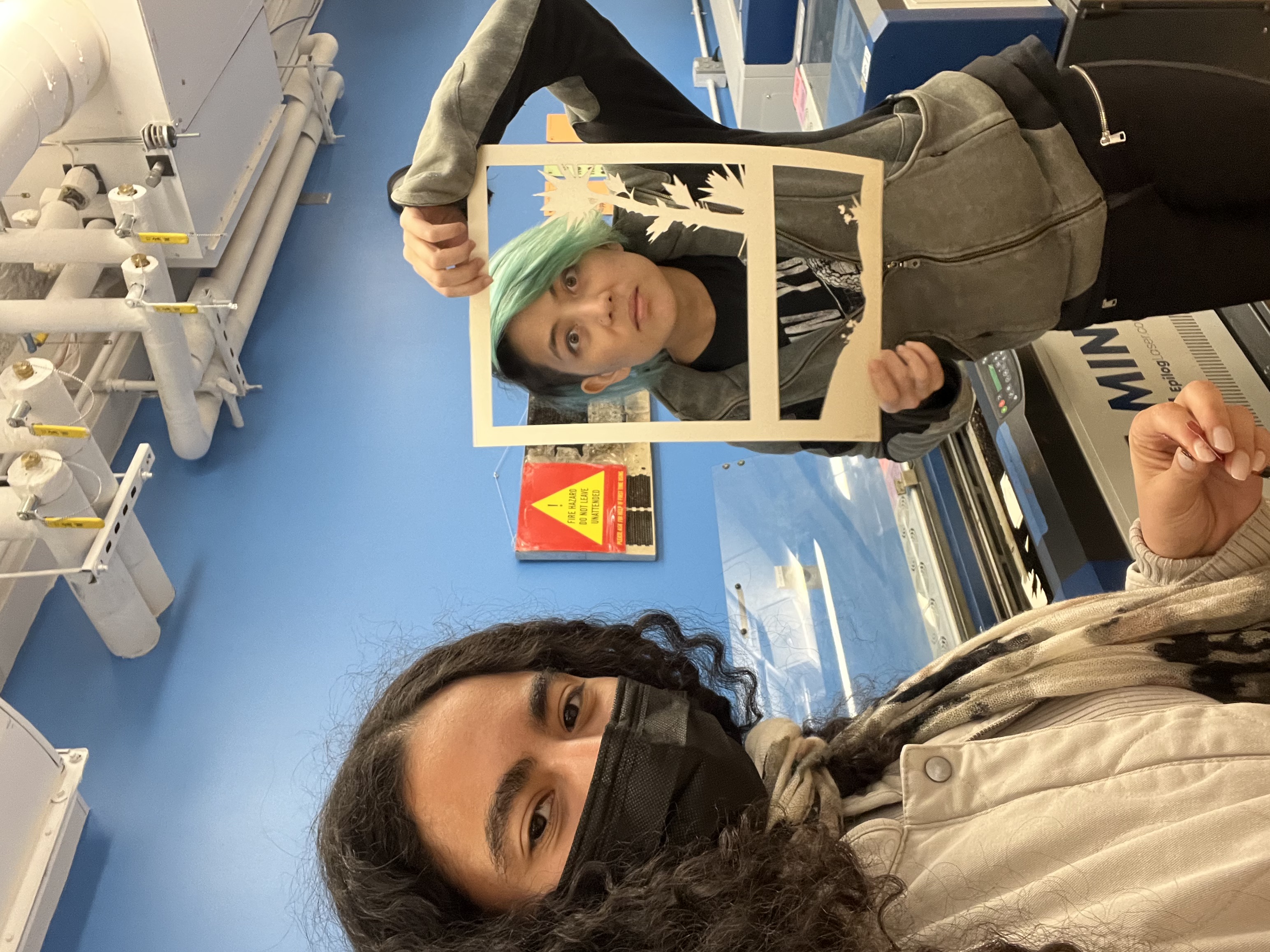 Photograph of two girls making funny faces while holding up laser cut papers like a picture frame