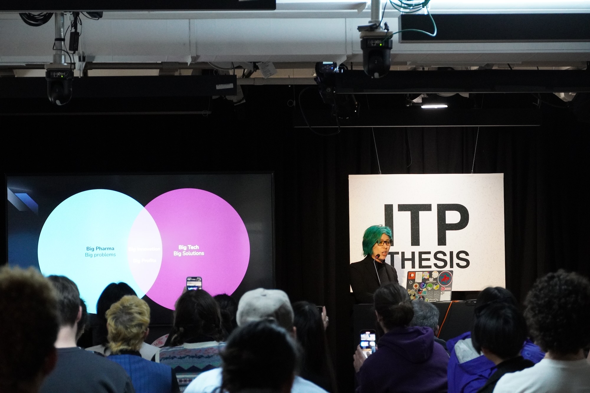 A photograph of a woman with green hair presenting a slide with a Venn diagram between "Big Pharma" and "Big Tech" showing the intersection as "Big Solutions"