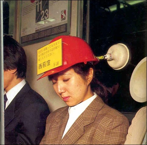 A photograph of a woman asleep in a train with a helmet and suction cup stuck to the window behind her, keeping her head from straying forward