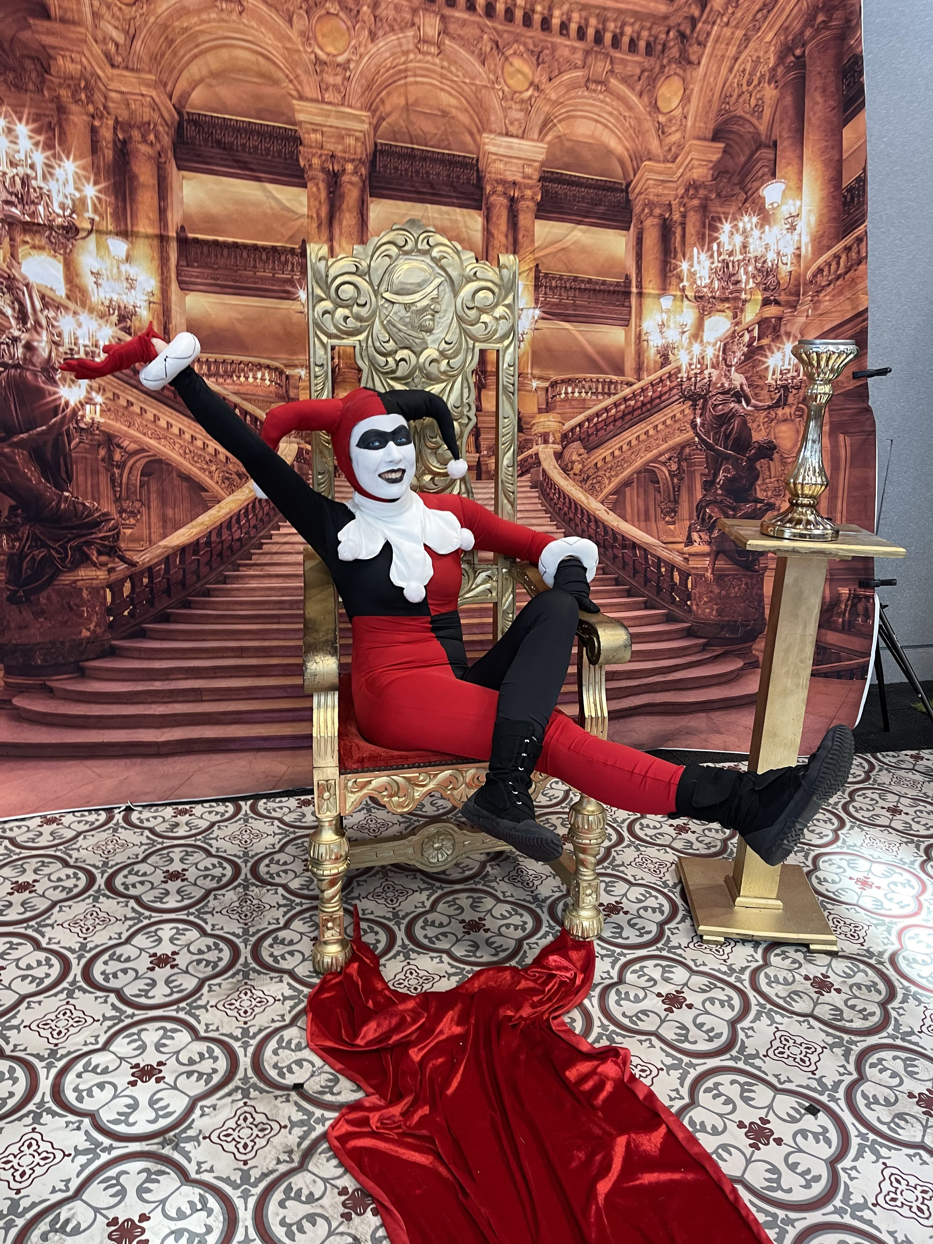 Photograph of a woman in a red and black harlequin outfit on a throne