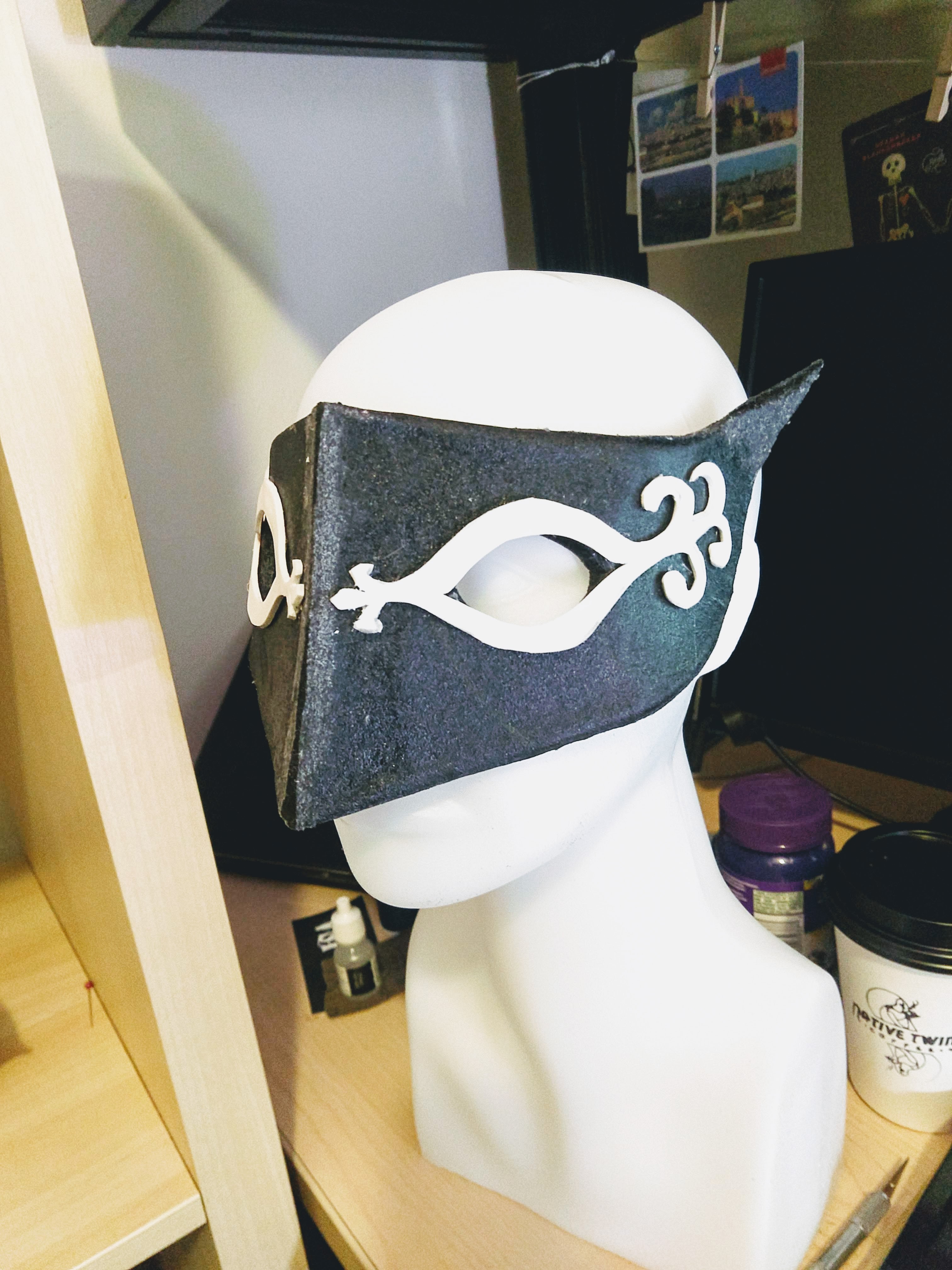 Photograph of a black mask with detailed designs around the eyes sitting on a head mannequin