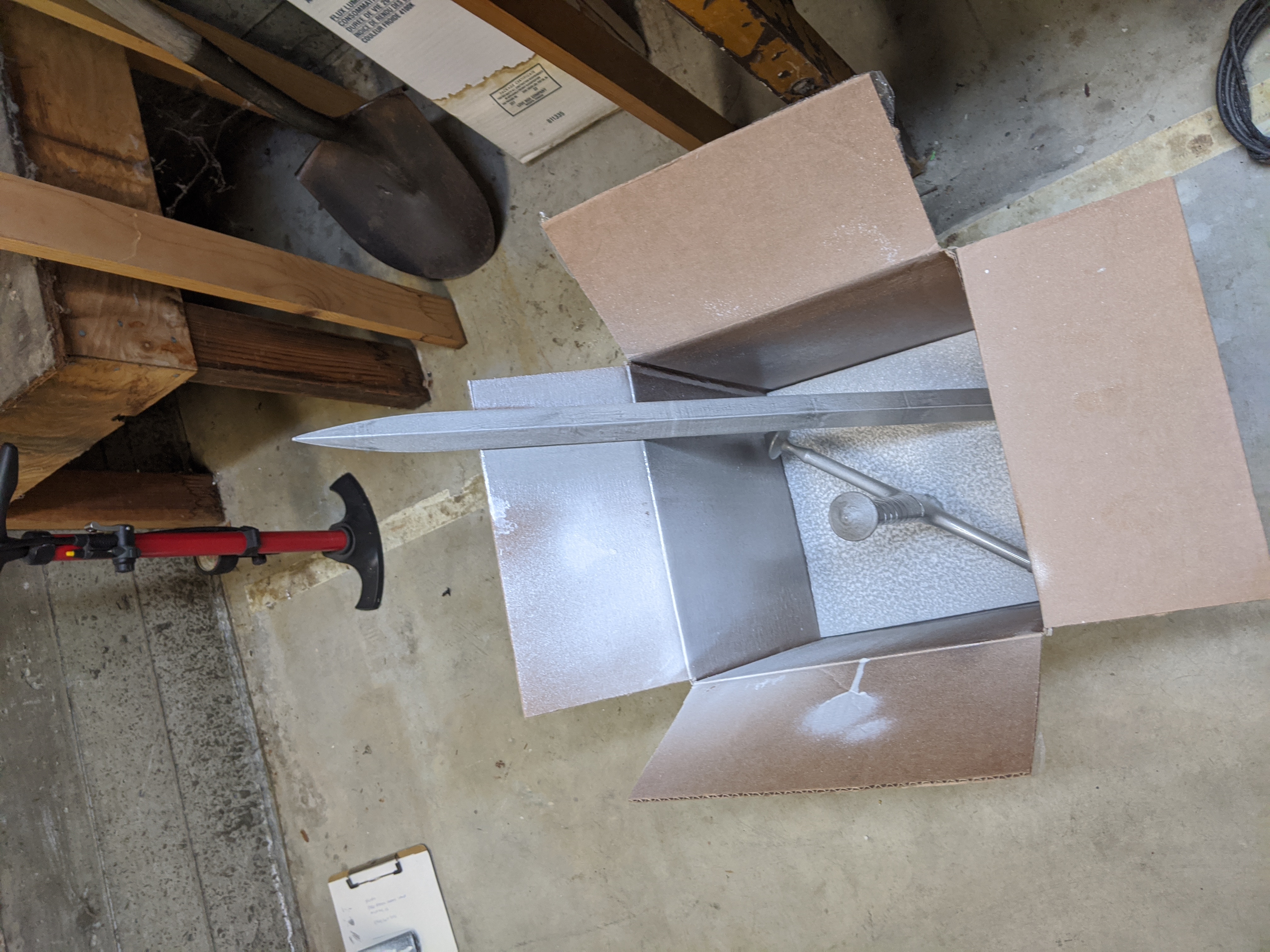 Photograph of pieces of a sword sitting in a box freshly coated with silver paint