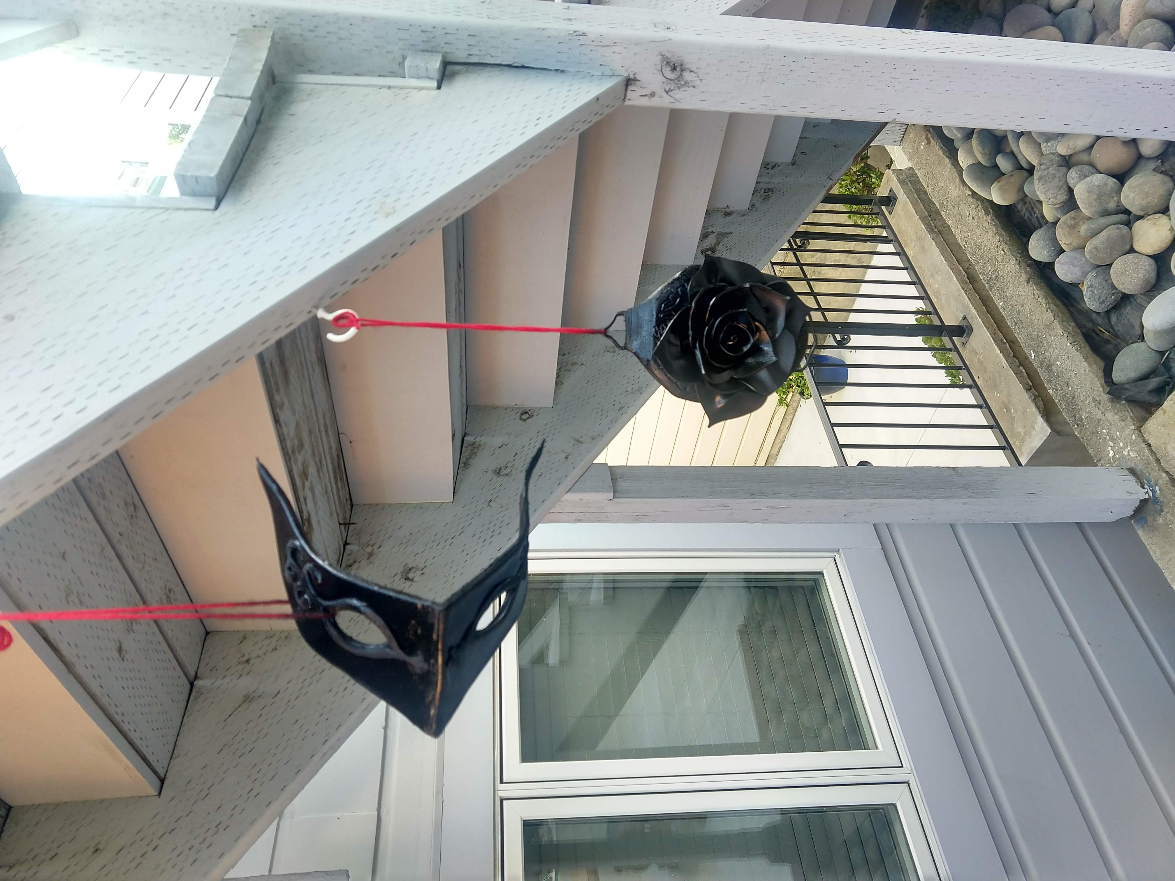 Photograph of a belt and mask covered in shiny black coating hanging from a staircase