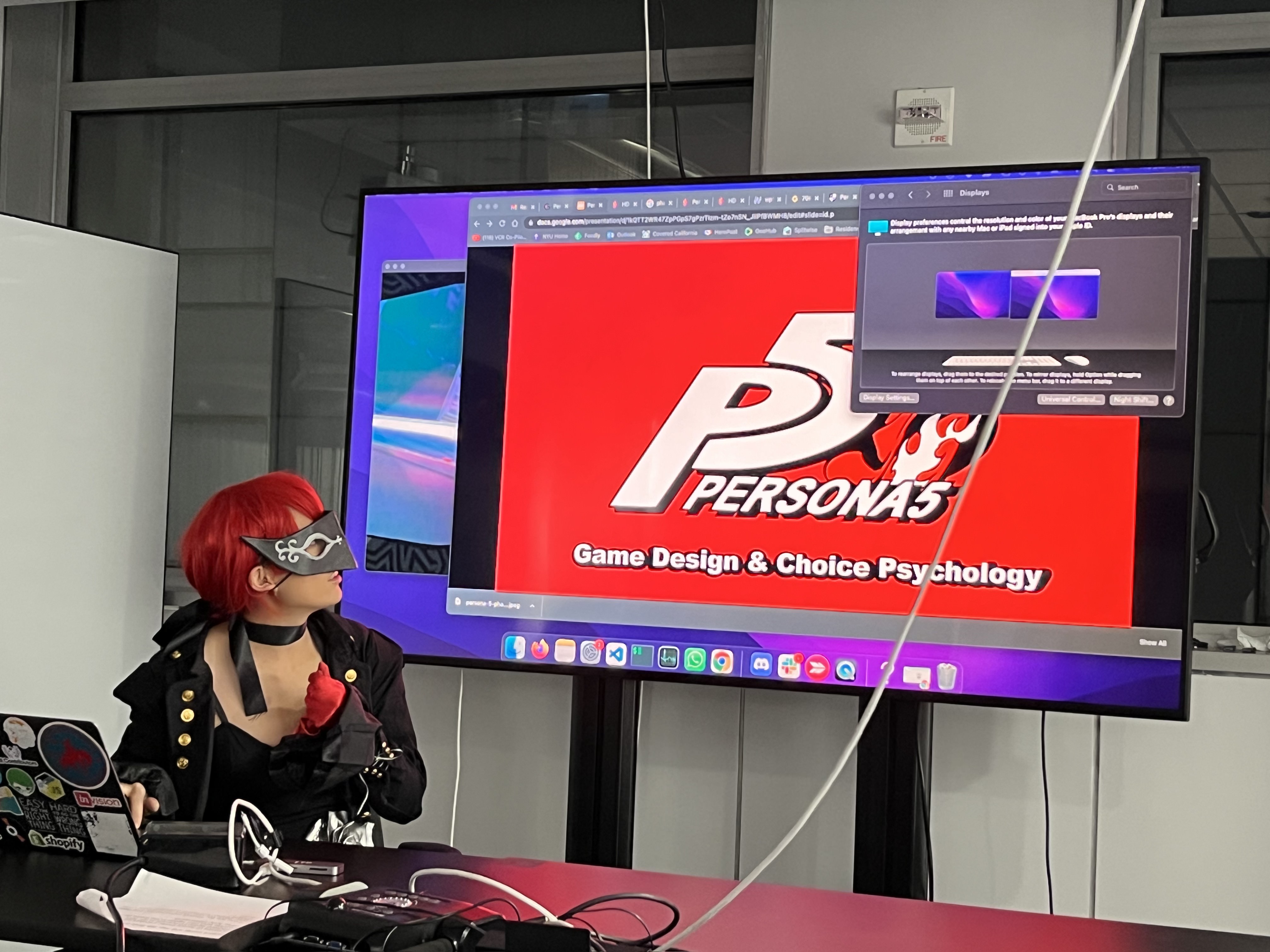 Photograph of a girl in a red wig looking at a screen that says "Persona 5"