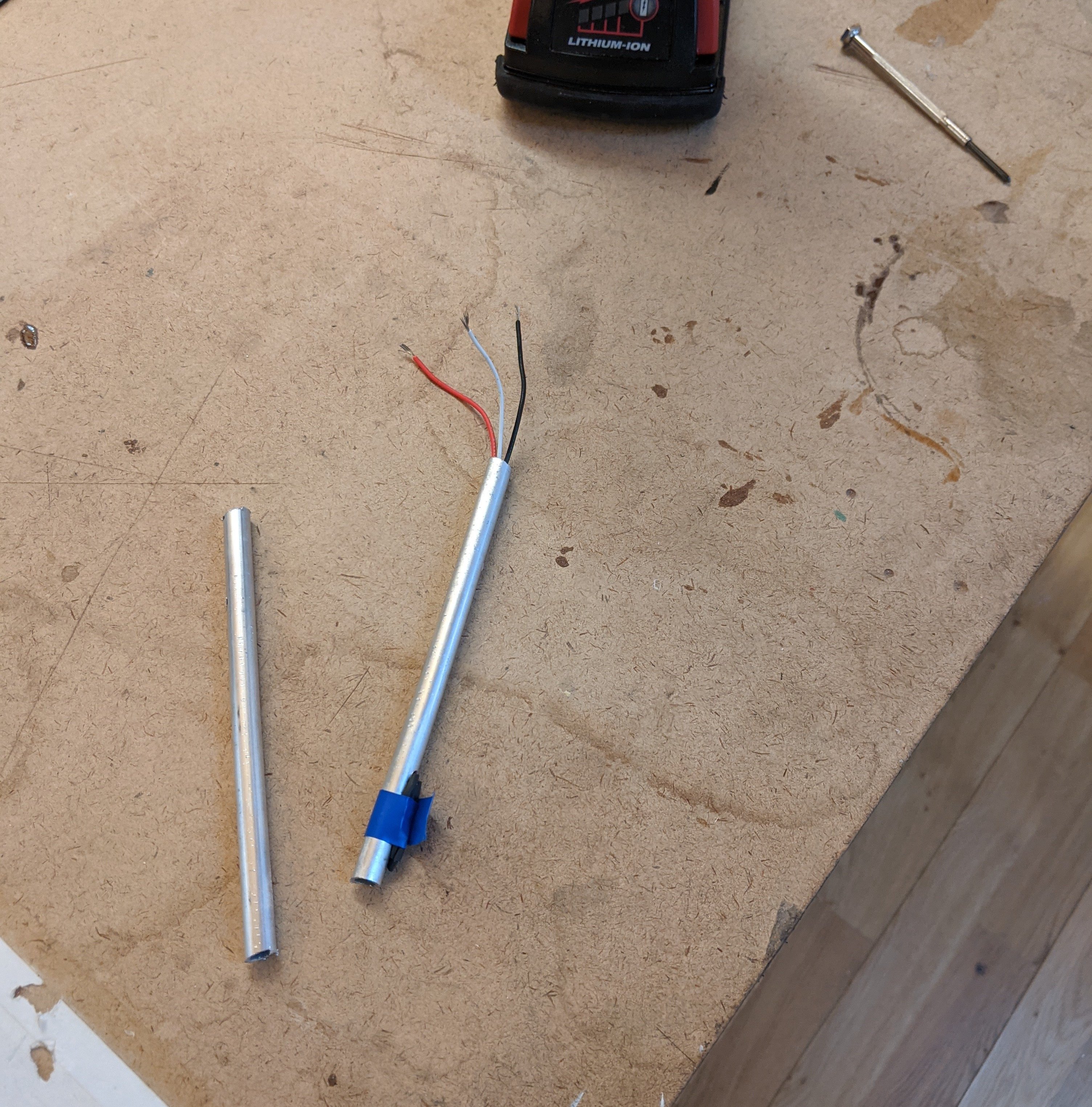 Photo of a messy workshop bench with a drill and metal tubes and wires