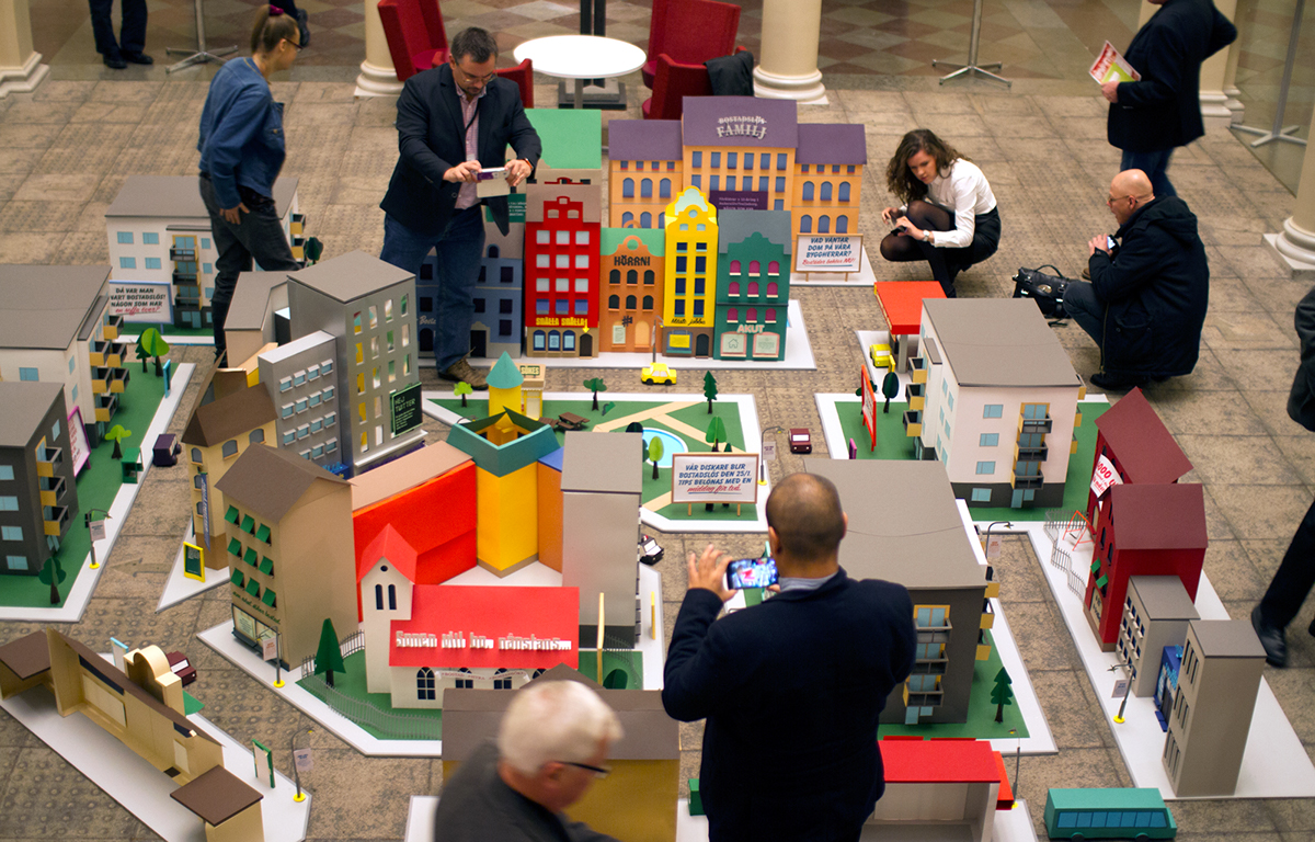 A photograph of people playing with a miniature scale model of a city