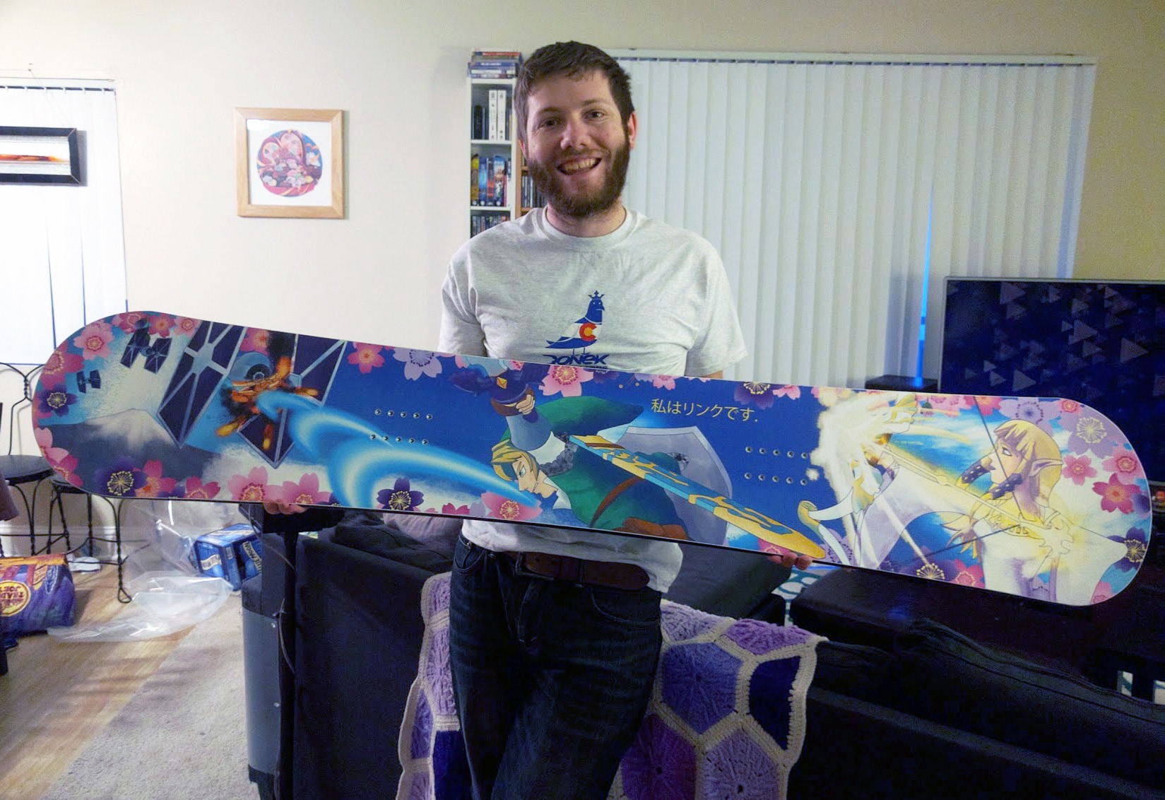 Photograph of a man holding up a Zelda and Star Wars themed snowboard